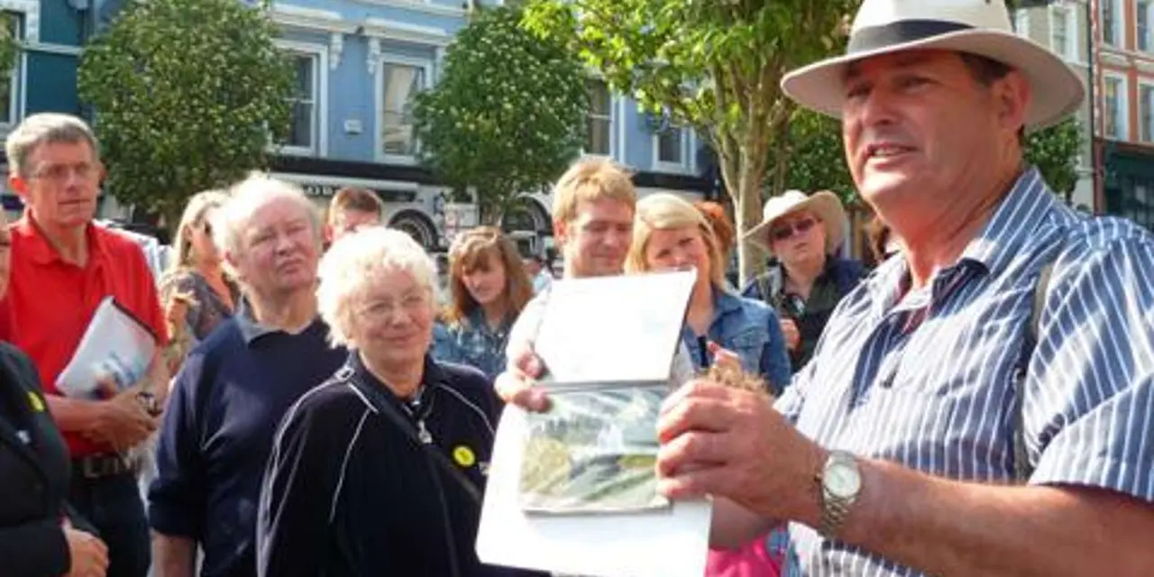 A guide holding up an old photograph to a group of visitors on a Cobh street