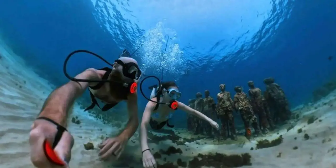 Two swimmers with air lines beside a ring of underwater statues