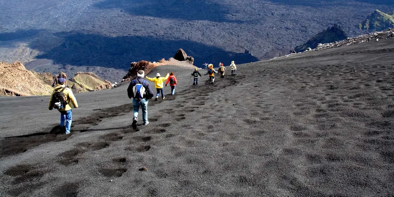 A line of trekkers climbing a black volcanic ash slope on Mount Etna