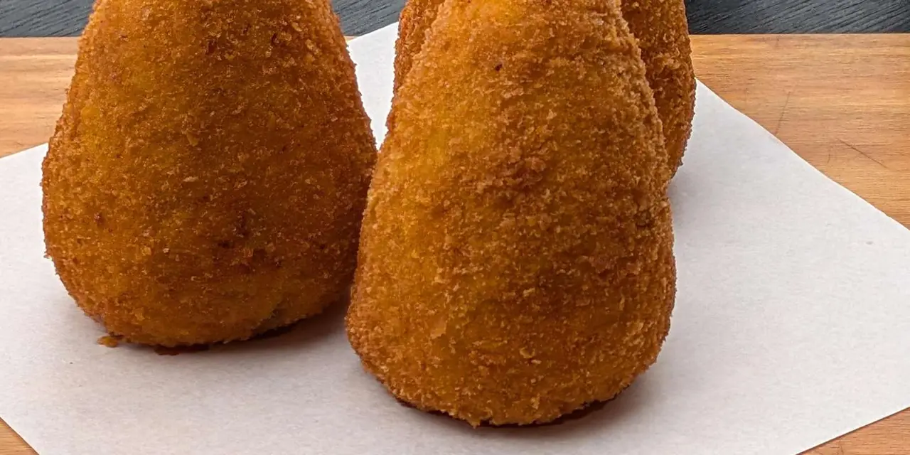 Three golden, cone-shaped arancini rice balls on a sheet of paper
