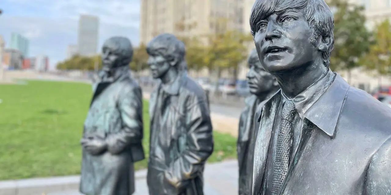 Close-up of the four bronze Beatles statues on the grass at Pier Head with the Royal Liver Building softly blurred behind