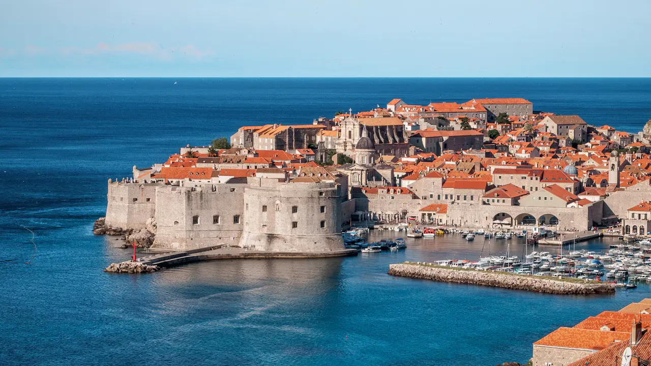 Dubrovnik's walled Old Town and its old harbor on the deep blue Adriatic, with stone forts and terracotta roofs under a clear sky