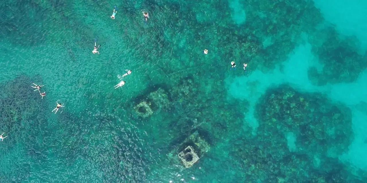 Aerial view of snorkelers floating above wreck remains on a pale sandy seabed