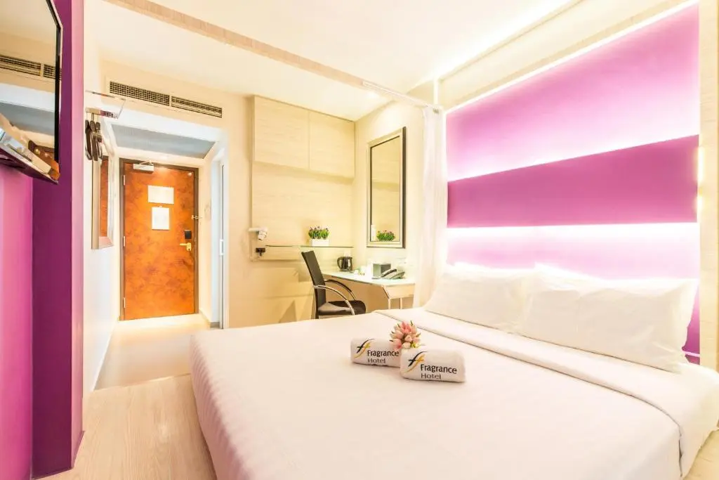 Double room at Fragrance Hotel - Viva with a queen bed, towels folded on the white linen, a lit purple feature wall and a small desk by the door