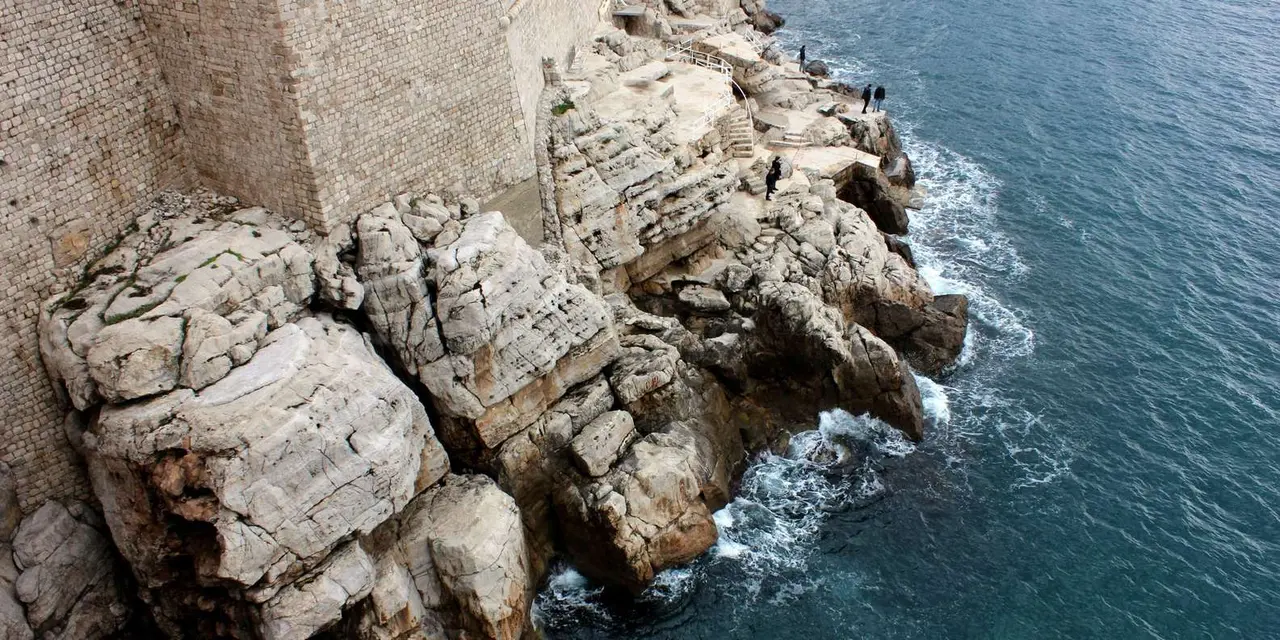 Pale limestone rocks and the base of the city walls rising straight out of the sea