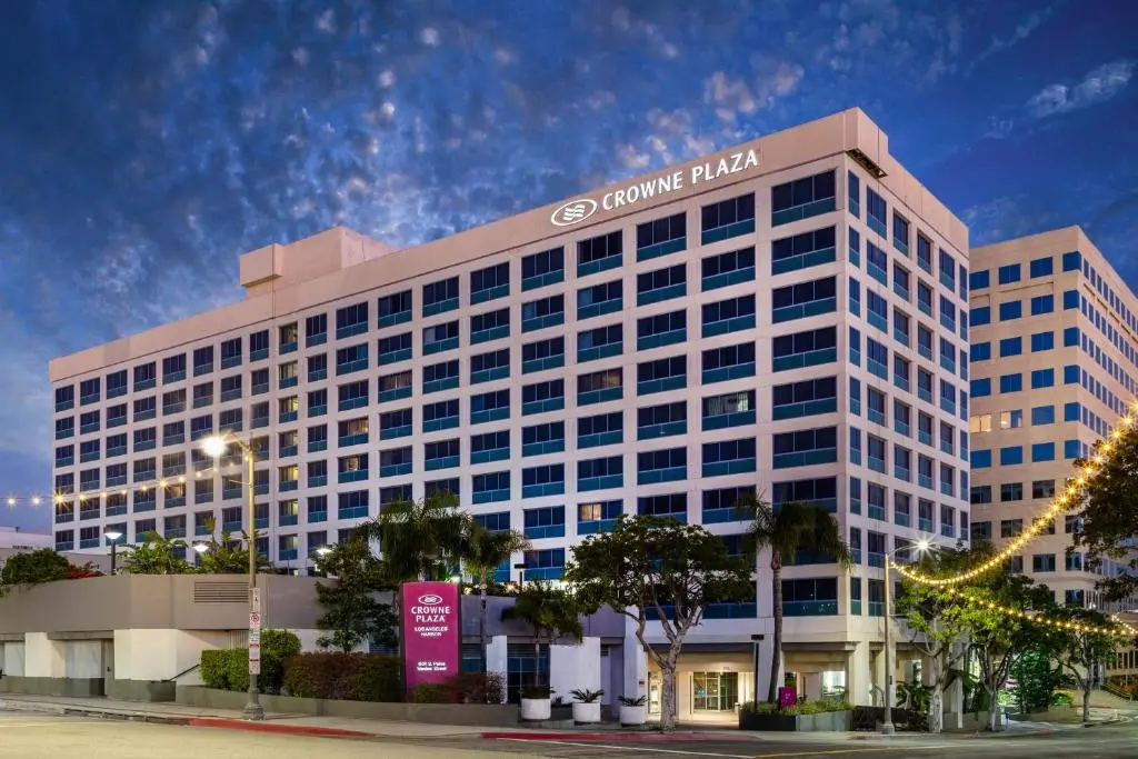 The white high-rise Crowne Plaza Los Angeles Harbor Hotel at dusk, palm trees and string lights along its entrance