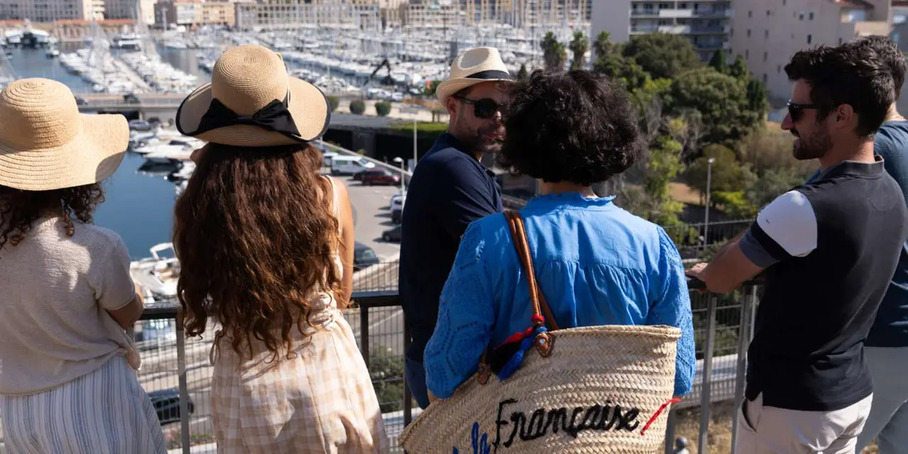 Visitors in sun hats on a terrace looking down at the boats in Marseille's Old Port