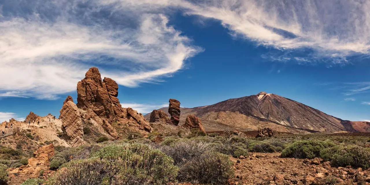 A straight empty road running through a volcanic landscape toward a mountain with wooden fences along both sides