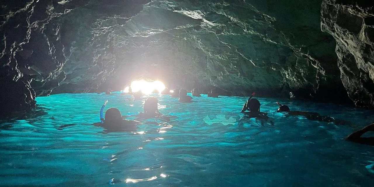 Swimmers floating inside a sea cave whose water glows turquoise from sunlight below