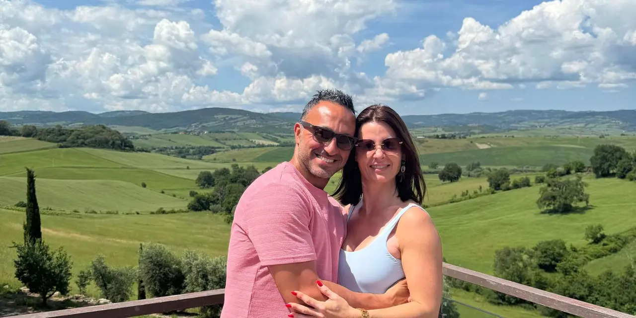 A couple posing on a terrace above rolling green Tuscan hills under a sky of white clouds