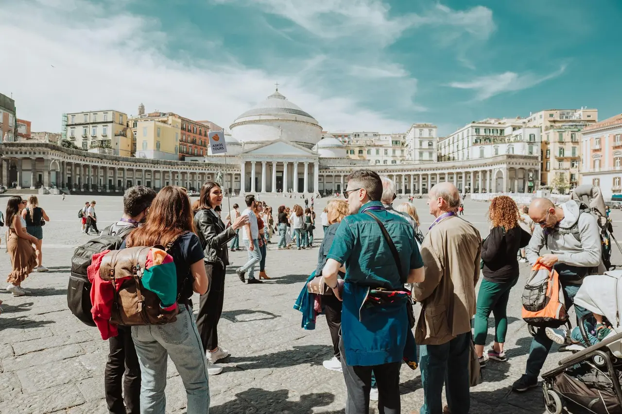 A tour group standing in the wide Piazza del Plebiscito, with the columned, domed church of San Francesco di Paola behind them