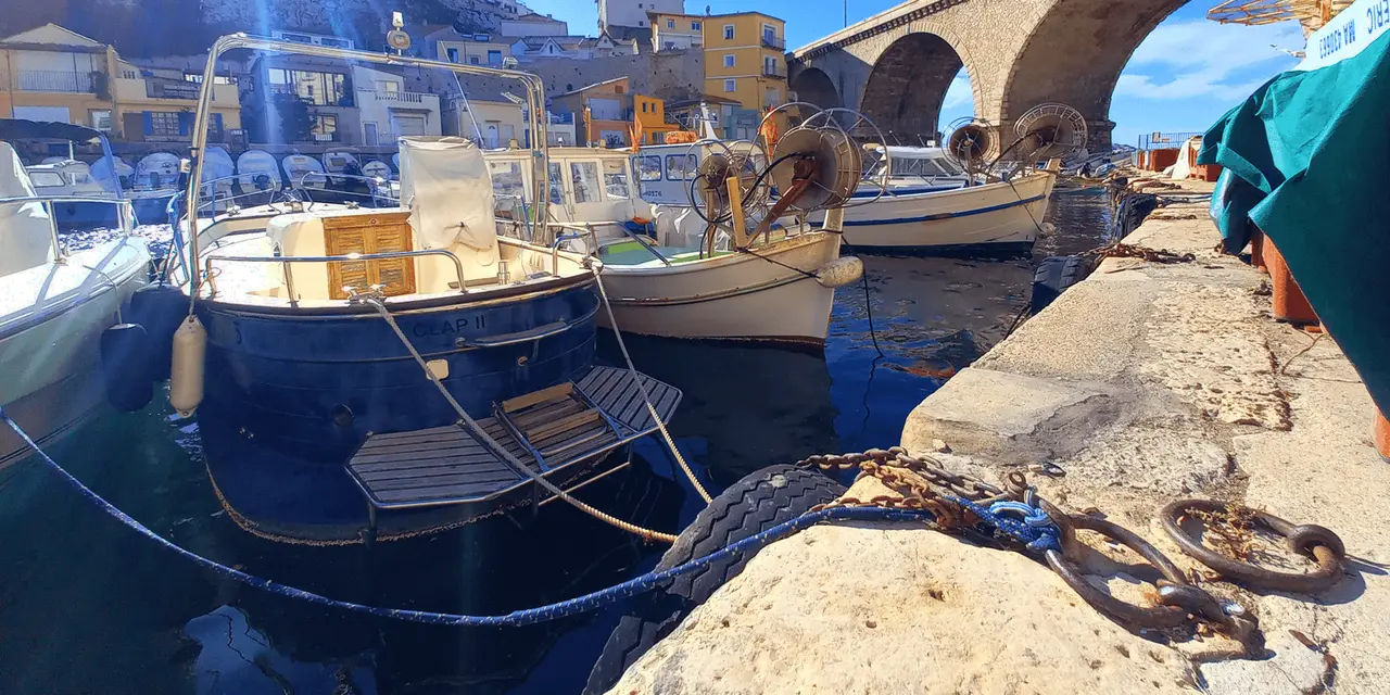 Painted fishing boats moored in the little harbour of Vallon des Auffes beneath its stone arch bridge