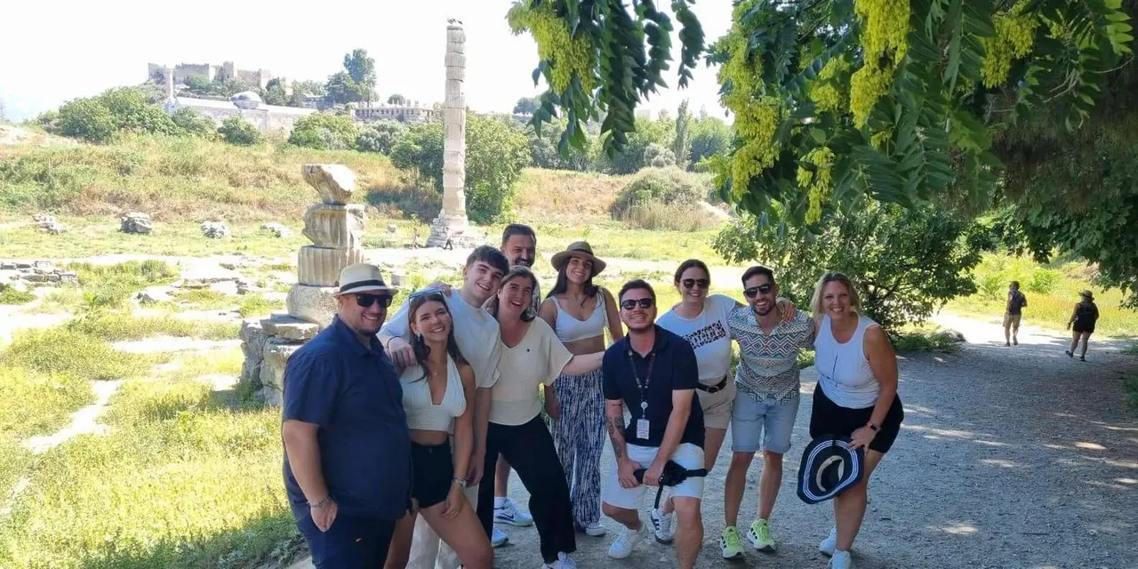 A tour group standing on green grass beside the single tall column of the Temple of Artemis