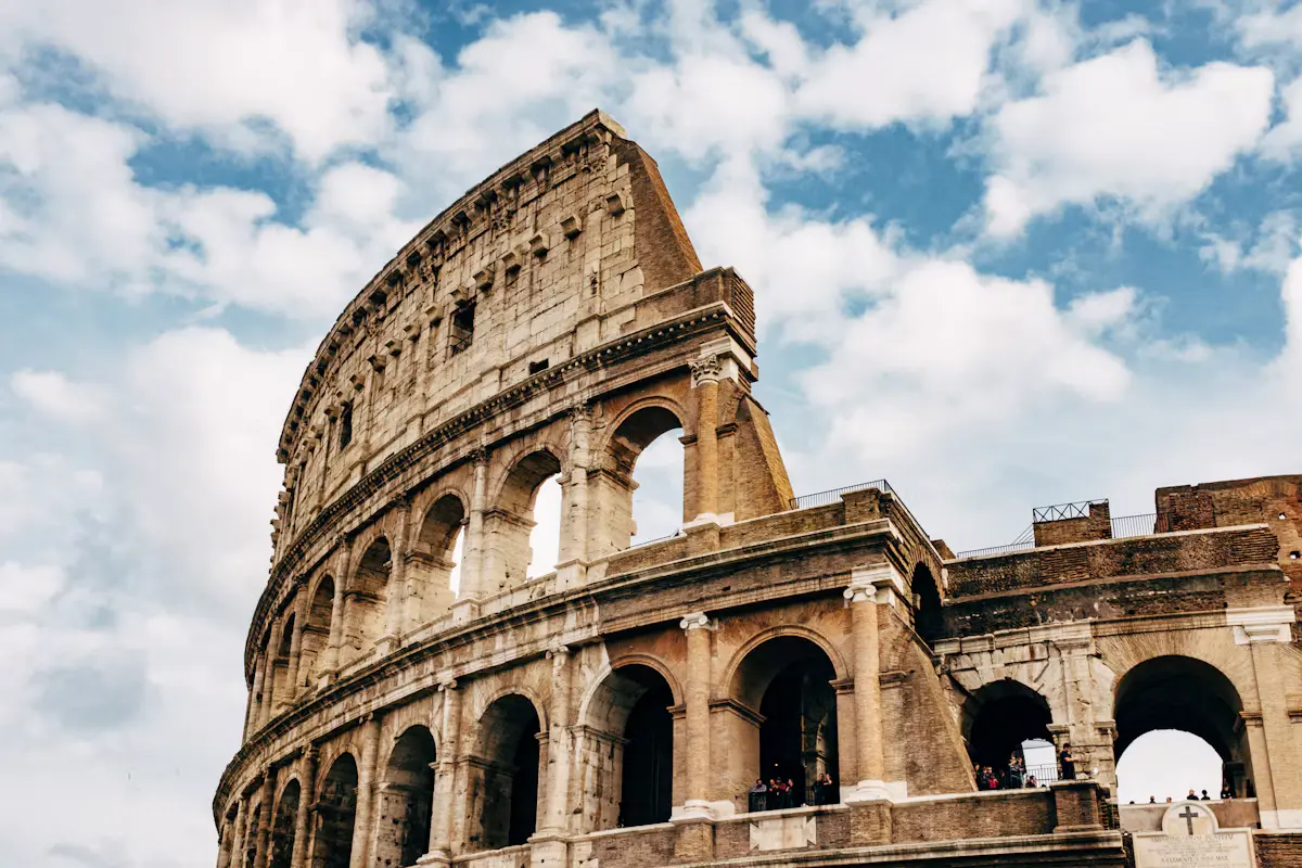 The Colosseum in Rome, about an hour from the port of Civitavecchia: its tall outer wall of stacked stone arches rising against a blue sky with white clouds