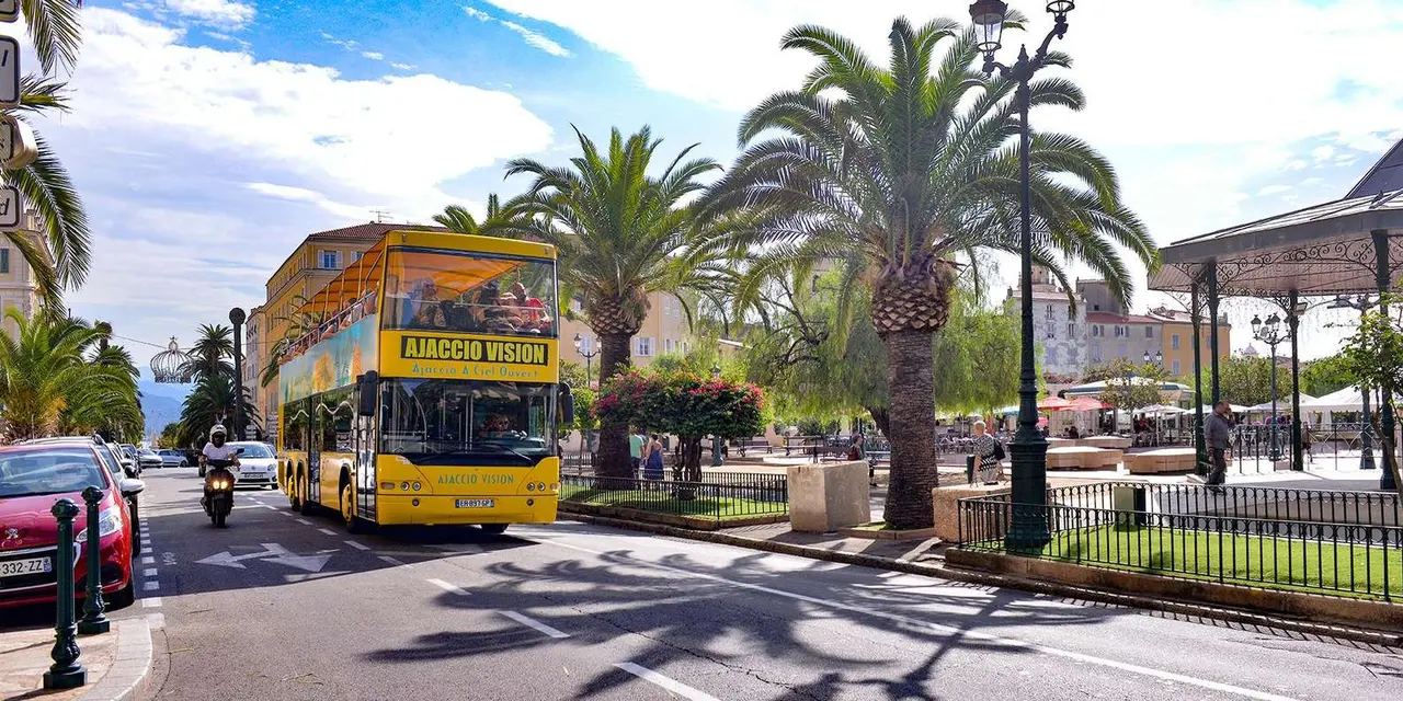 A yellow open-top sightseeing bus parked beside palm trees on a sunny square