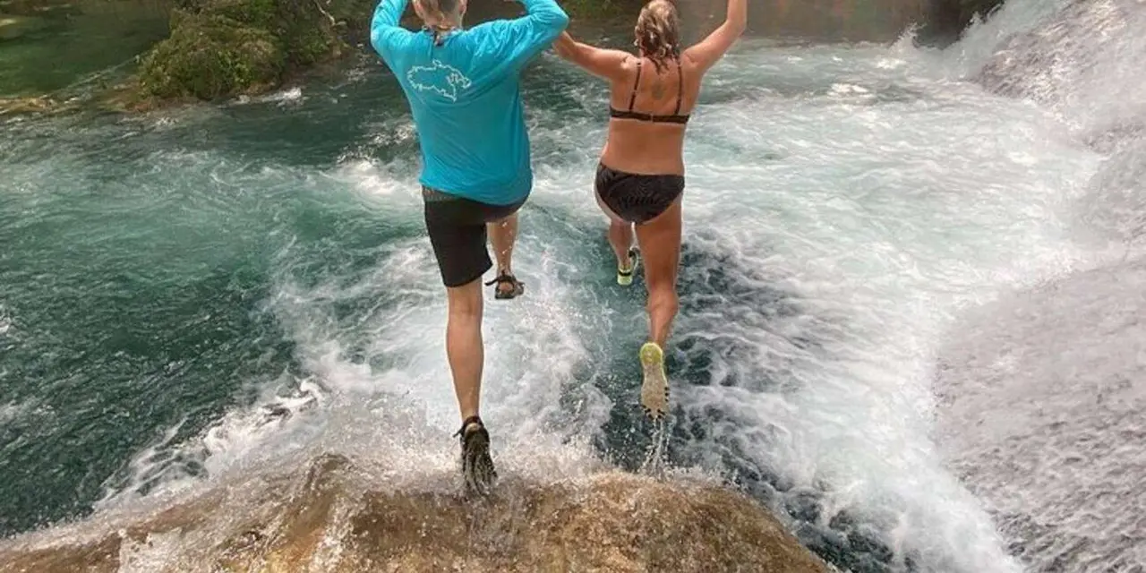 Two people wading across white-water rapids in a river