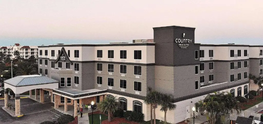 The five-storey Country Inn & Suites building at dusk, grey and cream with a rooftop sign, a covered entrance and palm trees in front
