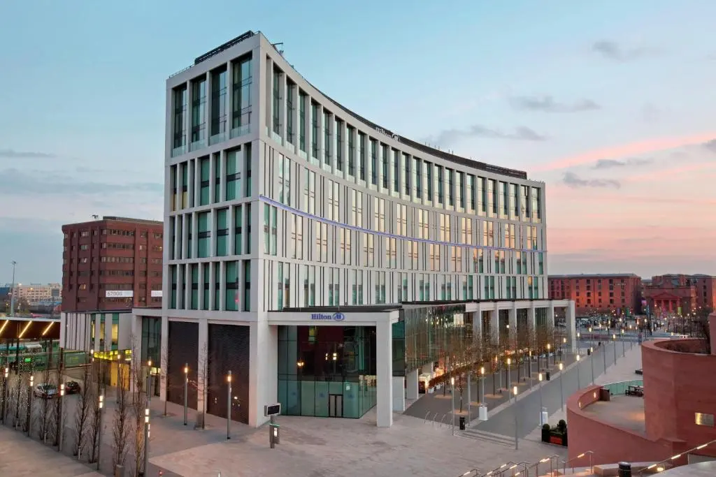 The curved glass front of the Hilton Liverpool City Centre at dusk, lit up beside Liverpool ONE