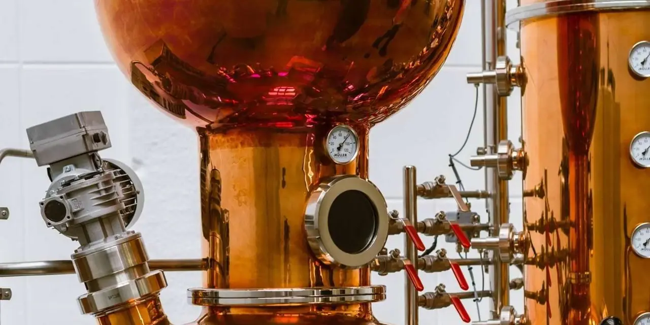 Copper distillation stills with pressure gauges and red-handled valves against a white tiled wall
