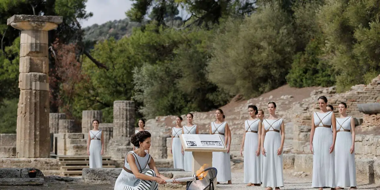 Women in white robes gathered at a stone altar in front of ancient columns at Olympia, as in the Olympic flame ceremony