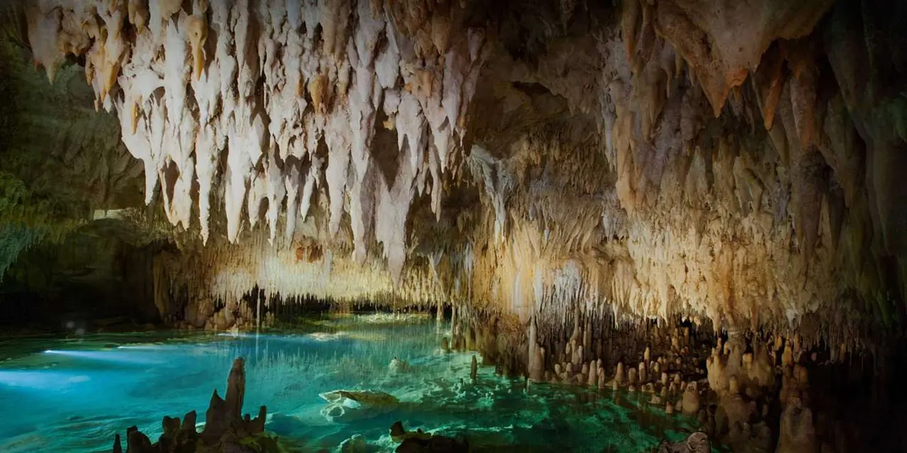 Stalactites hanging from a cave ceiling above a pool of clear blue-green water