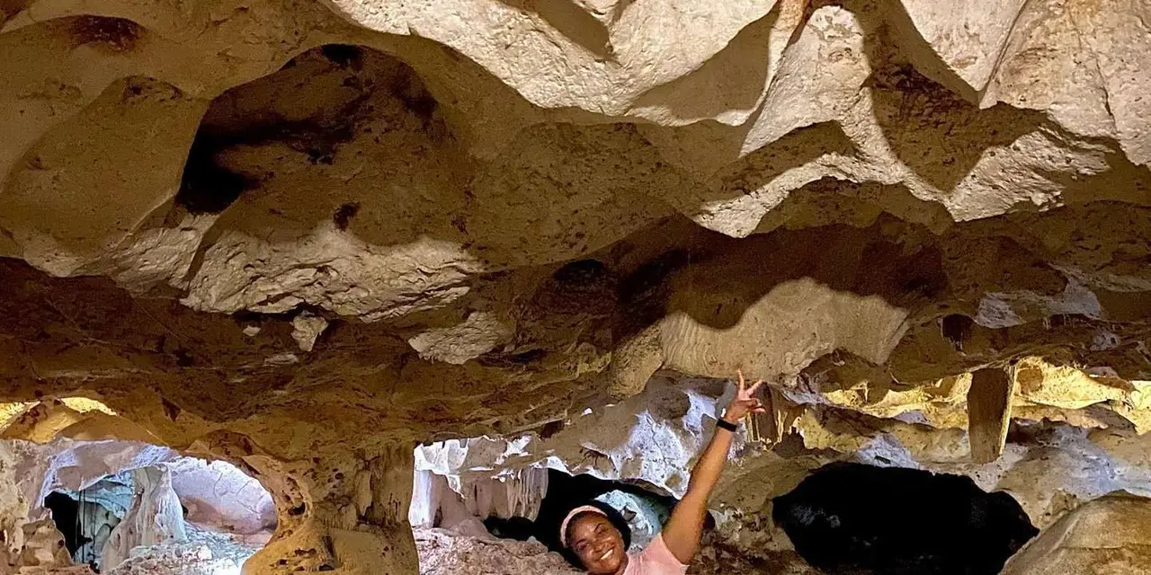A visitor posing inside a limestone cave chamber with pale rock walls