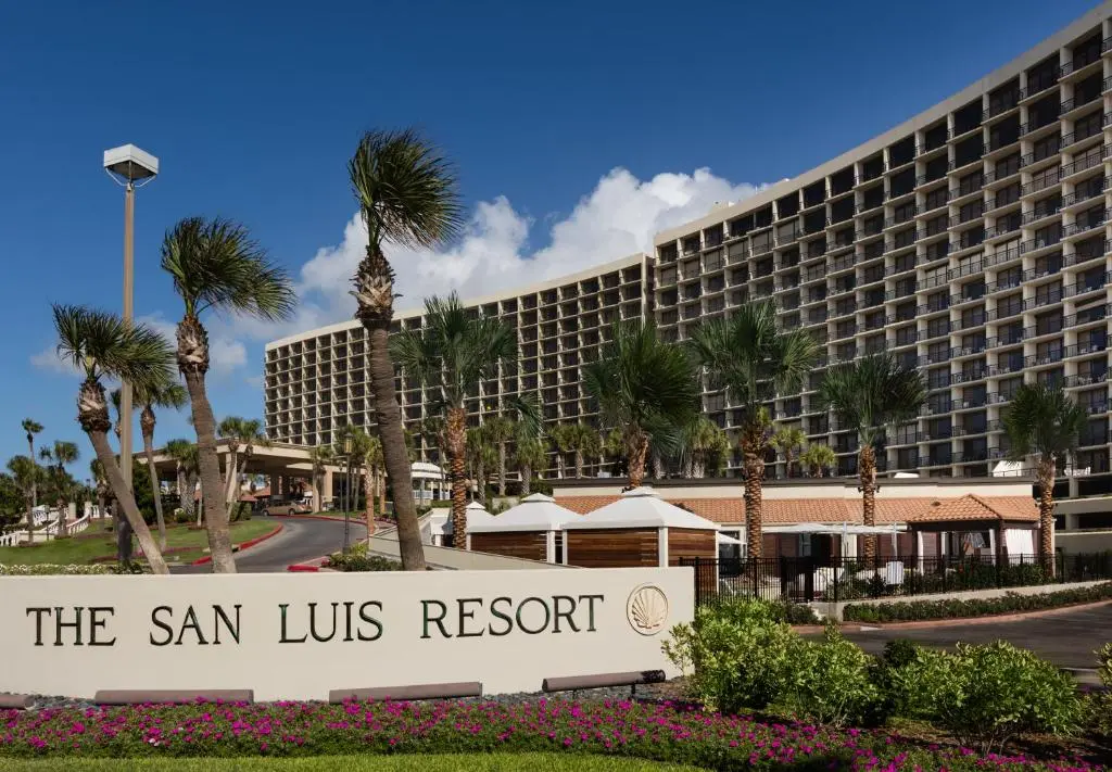 The San Luis Resort's curved beachfront tower behind palm trees and the entrance sign