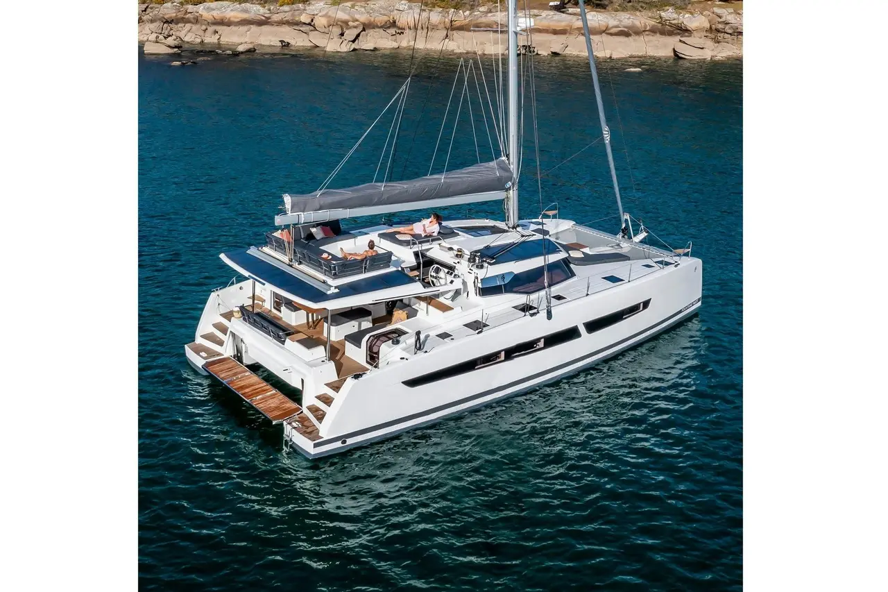A white sailing catamaran at anchor on deep blue water near a rocky shore