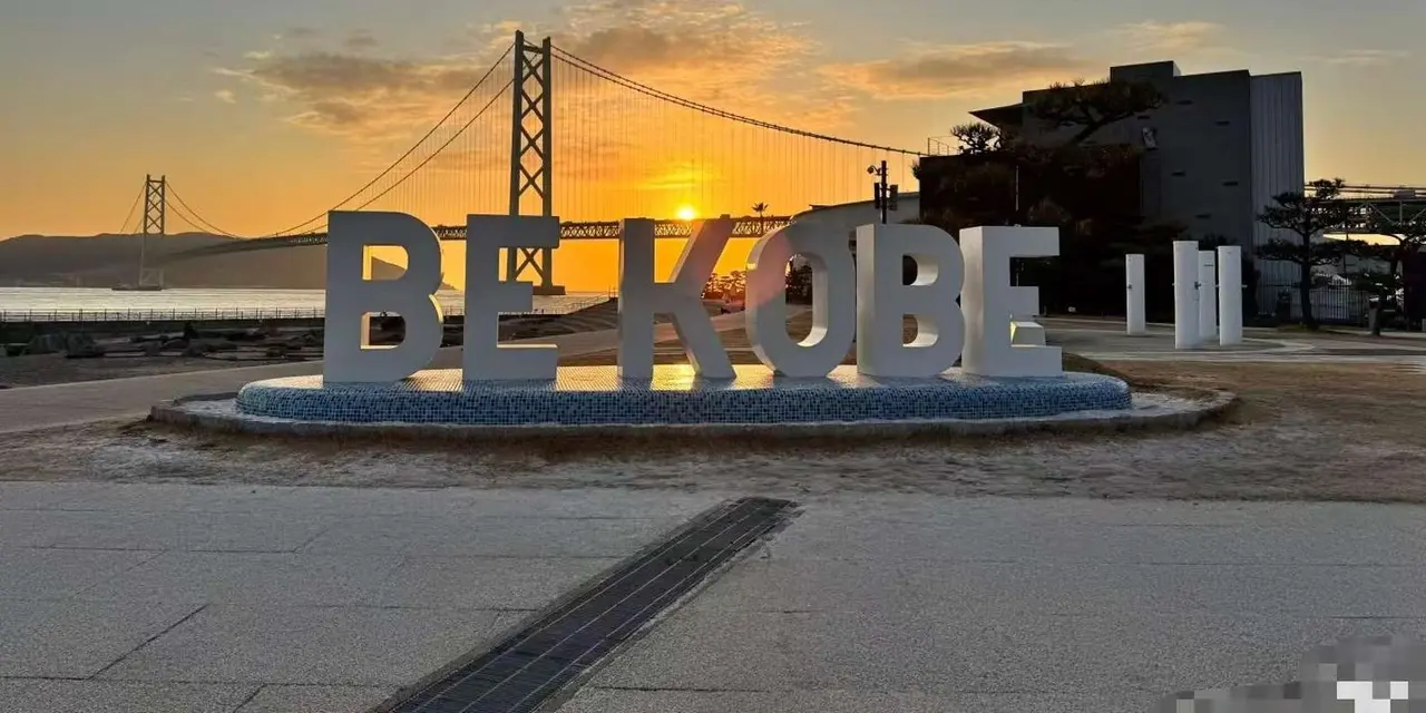The BE KOBE letters at sunset with the Akashi Kaikyo Bridge on the horizon