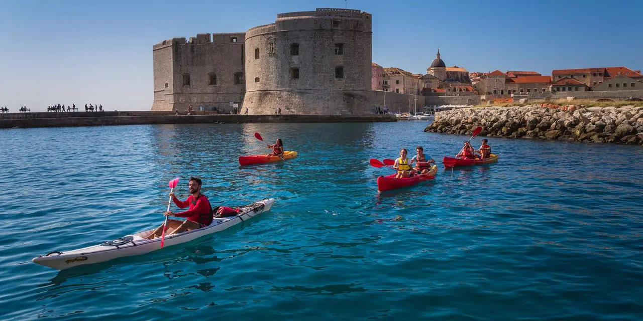 Kayakers in red kayaks paddling across clear blue water below Dubrovnik's Fort St. John