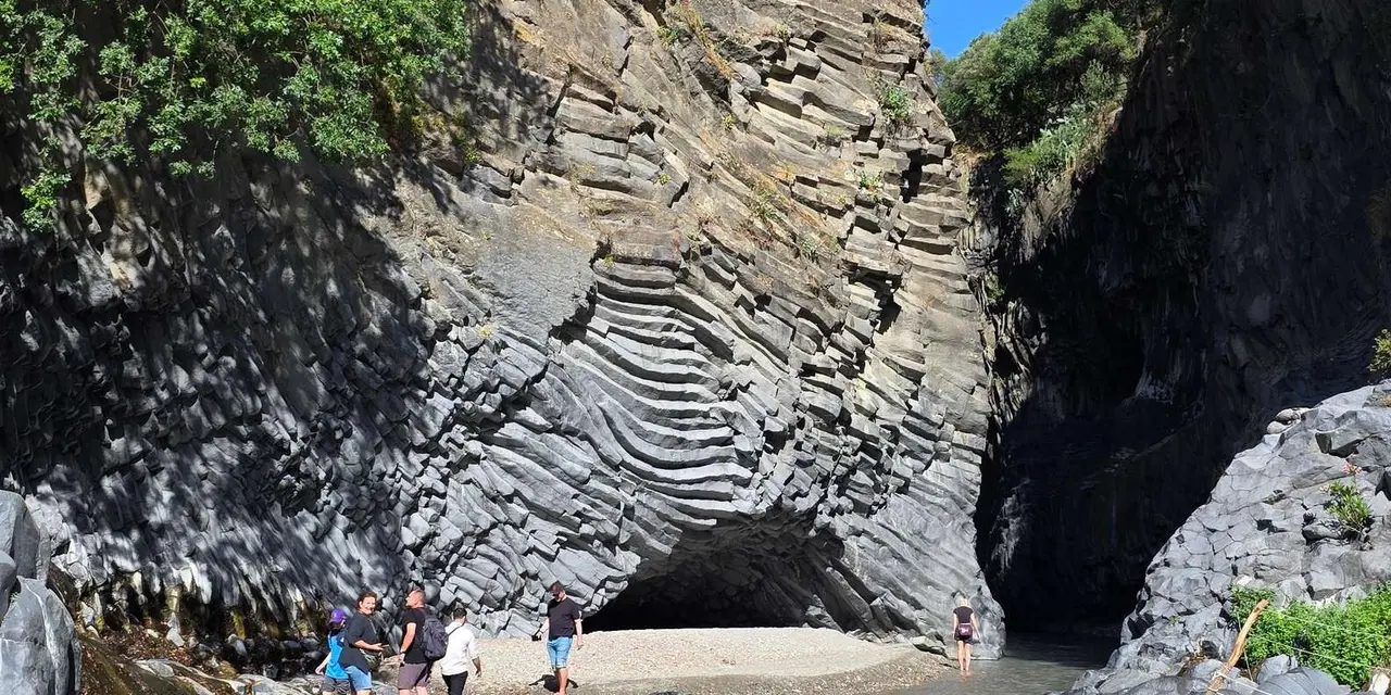 Layered grey basalt walls of the Alcantara Gorge with a few visitors at its base