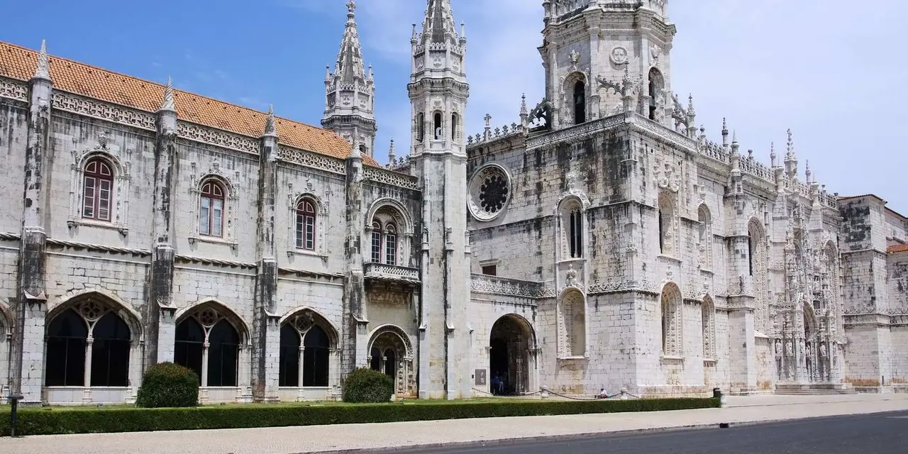 The pale carved stone facade and towers of Jerónimos Monastery under a blue sky