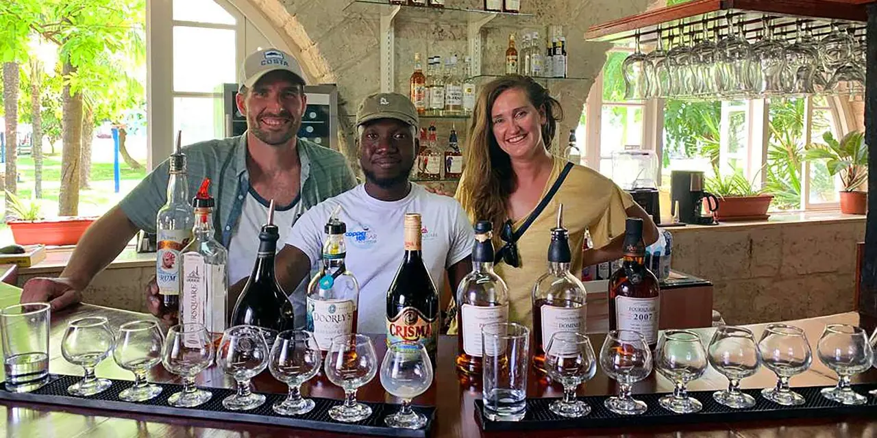 Three guides smiling behind a bar lined with rum bottles and tasting glasses