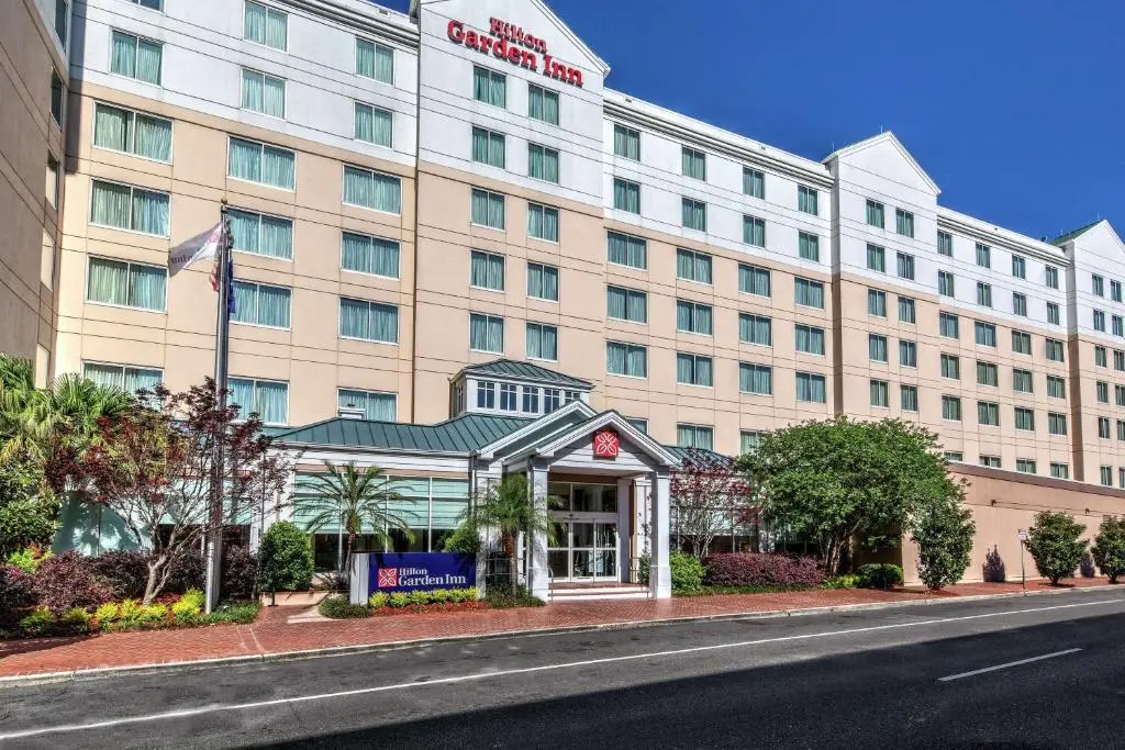The Hilton Garden Inn's cream-coloured building and columned entrance on South Peters Street, with palms and flowering shrubs out front