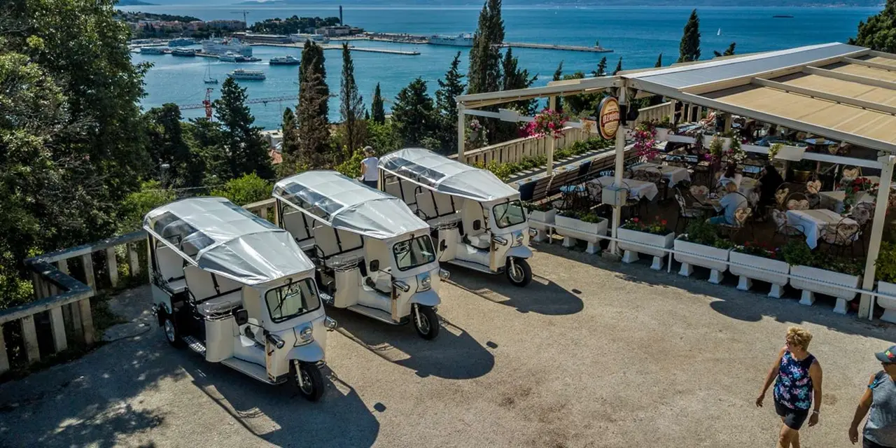Three white electric tuk-tuks parked on a terrace above Split's harbour