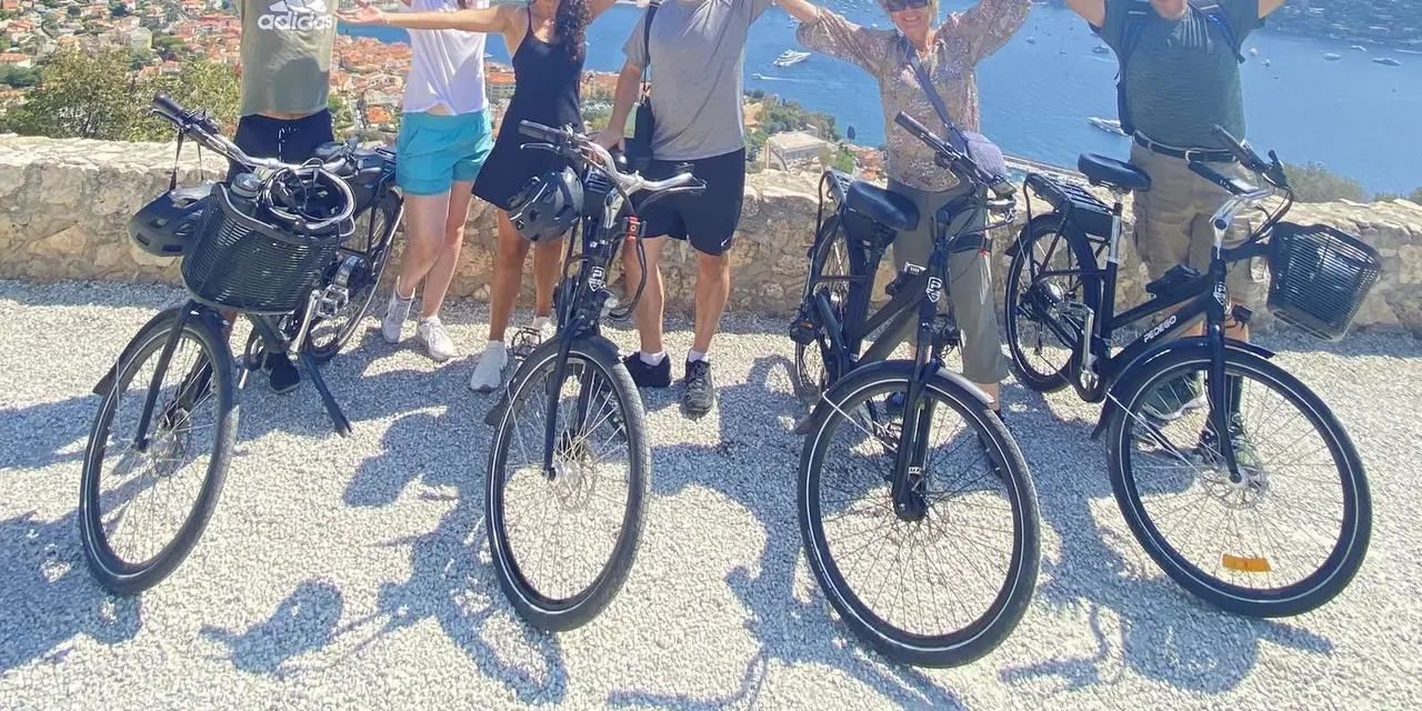 A group of cyclists cheering beside their e-bikes at a viewpoint over the sea