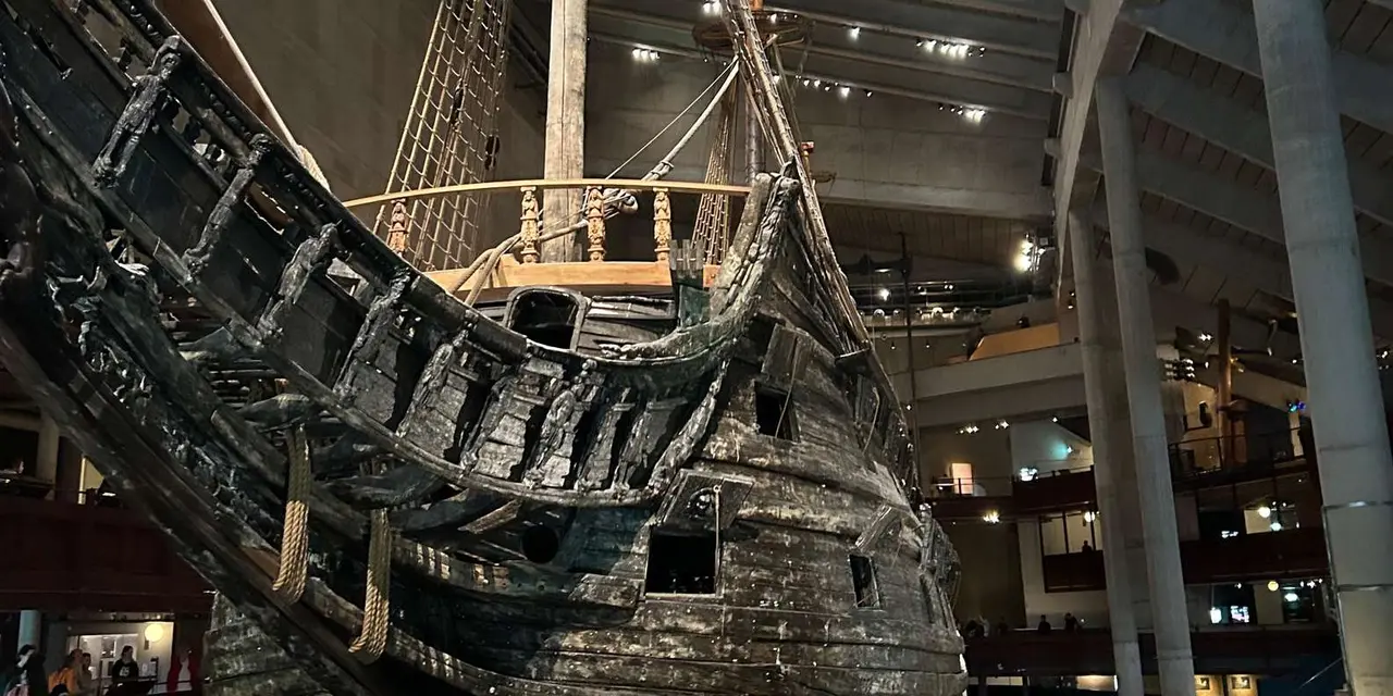 The dark timber hull of the Vasa warship with its rigging, lit inside the museum hall
