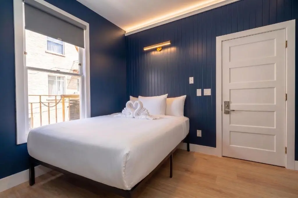 A San Remo Hotel room with a white double bed against navy panelled walls and a tall window