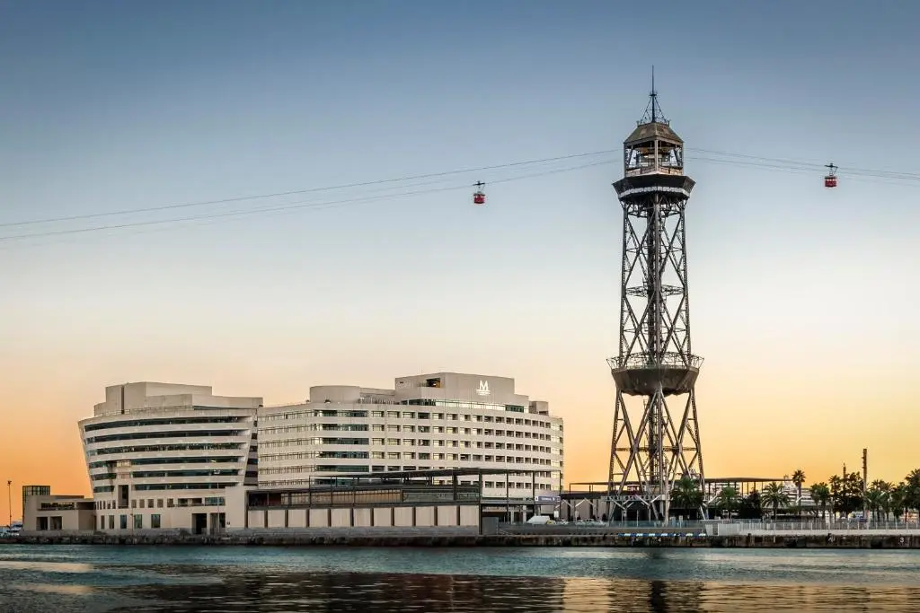 The curved white Eurostars Grand Marina building at the World Trade Center on Moll de Barcelona, beside the harbour cable-car tower, at dusk