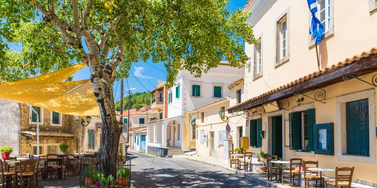 Cream village houses with green shutters and café tables along a narrow street