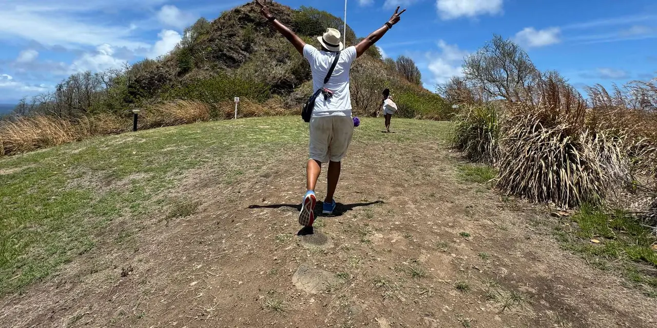 A visitor with arms raised on a grassy hilltop path