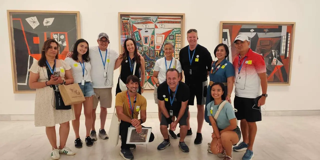 A tour group posing together in a bright gallery in front of three large, colourful Picasso paintings
