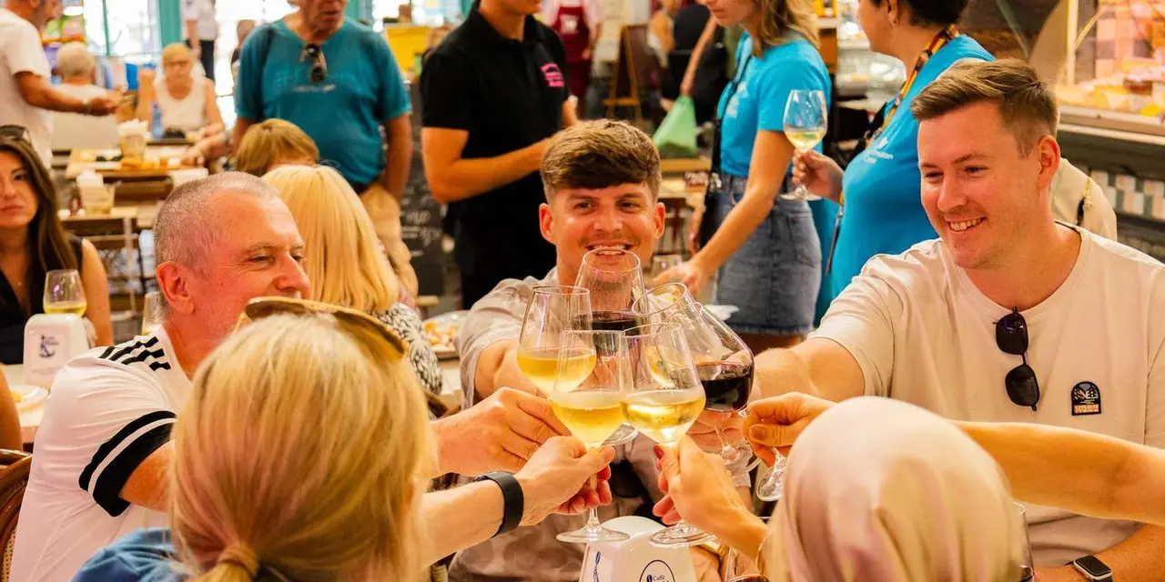 A group raising glasses of white and red wine around a crowded food-market table