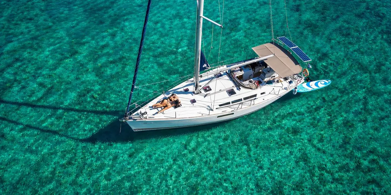 Aerial view of a white sailboat with people on deck over clear turquoise water