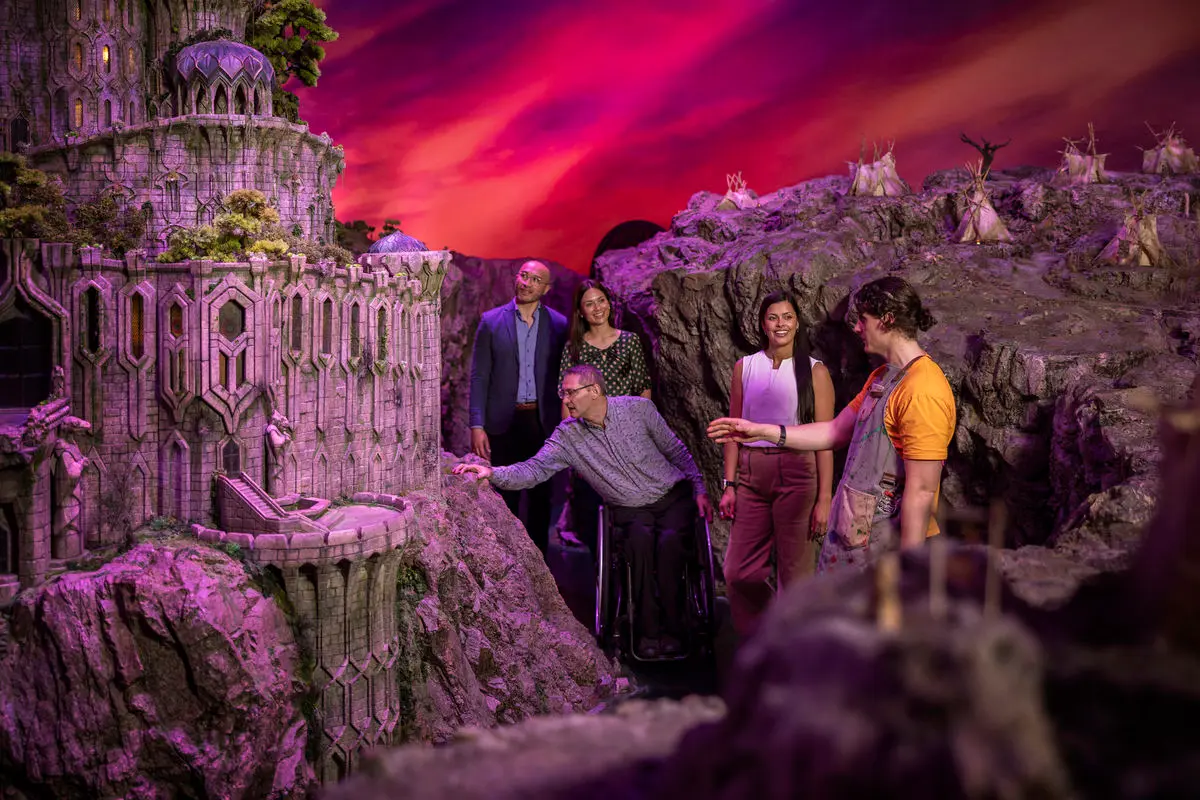 Visitors and a host standing among purple-lit fantasy castle sets inside Wētā Workshop Unleashed