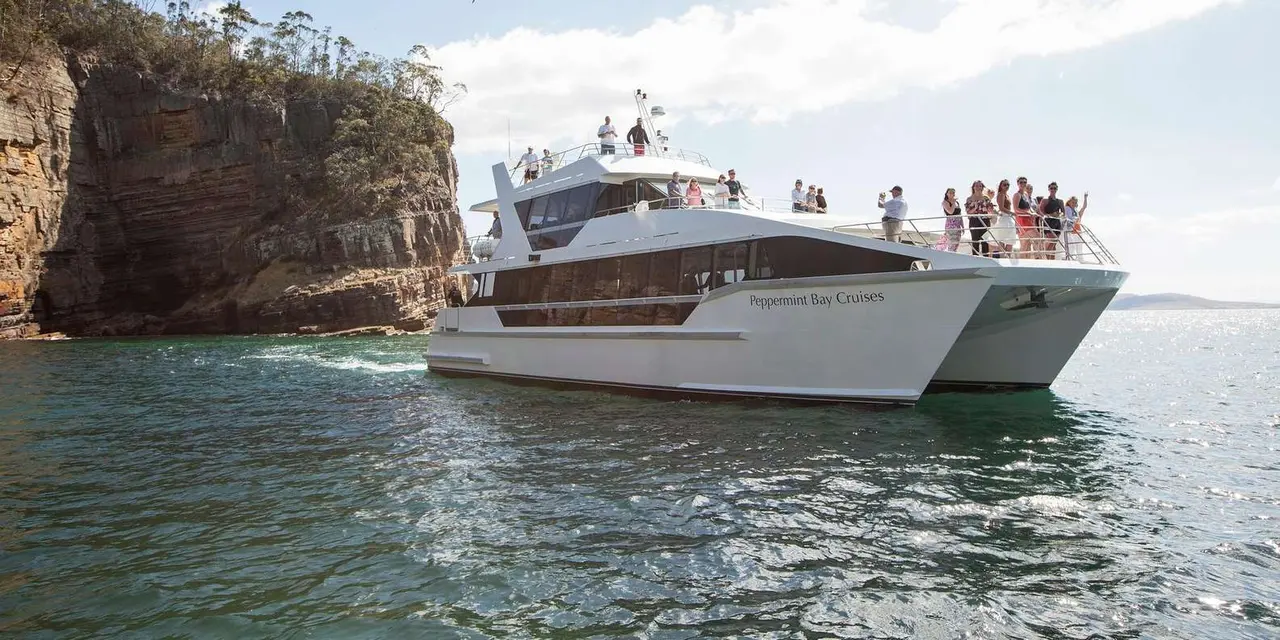 A white two-deck catamaran with passengers on its top deck on the Derwent