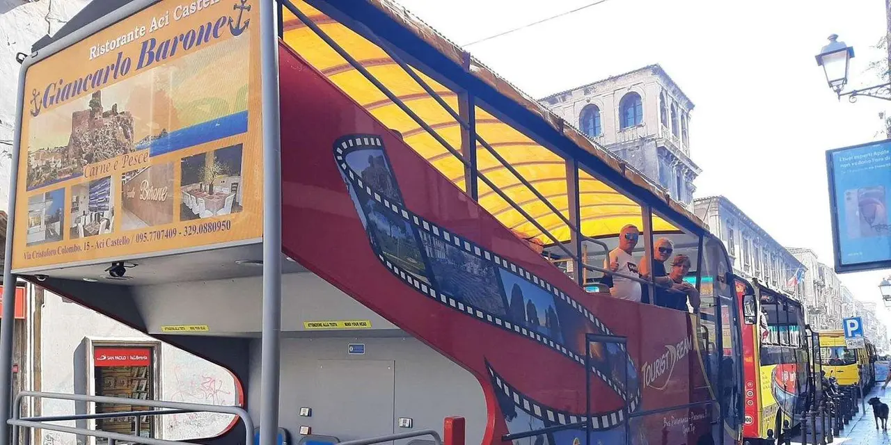 A red double-decker sightseeing bus in front of a Catania building