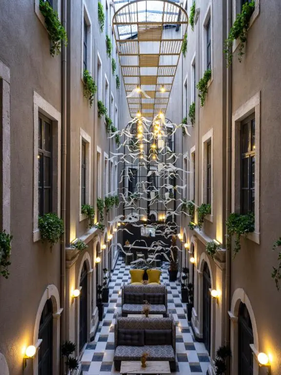 Glass-roofed atrium at Ferman Port Hotel, with balconies trailing plants around a lounge on a black-and-white tiled floor
