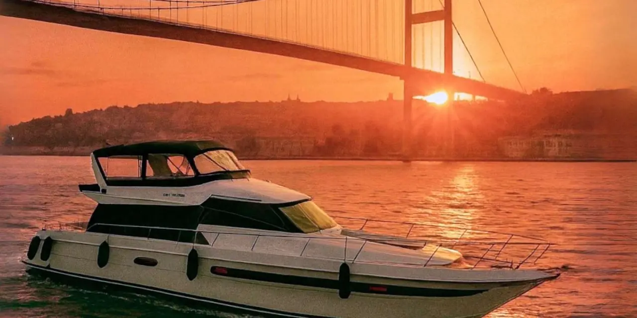 A white motor yacht cruising the Bosphorus at sunset with the Bosphorus Bridge silhouetted behind