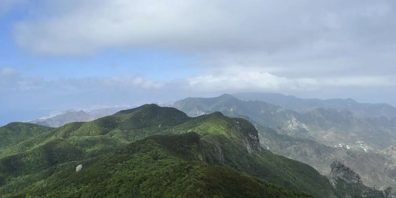 Green forested ridges of the Anaga mountains under cloud, with the coast visible in the far distance